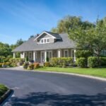A view of a well-maintained house with a curved asphalt driveway under a clear blue sky.