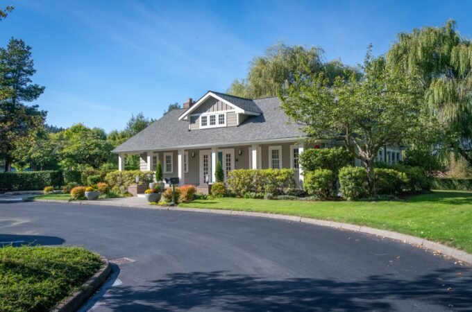 A view of a well-maintained house with a curved asphalt driveway under a clear blue sky.