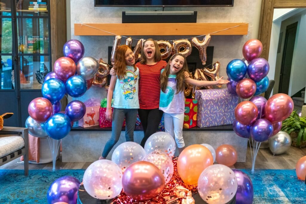 Three girls celebrating a birthday with metallic balloons and a 'Happy Birthday' sign.
