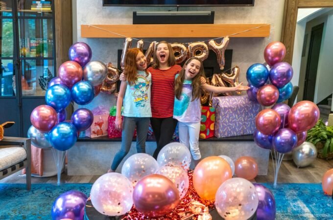 Three girls celebrating a birthday with metallic balloons and a 'Happy Birthday' sign.
