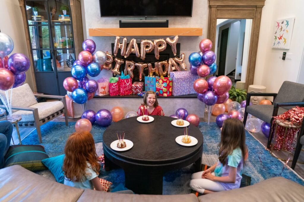 A family gathers around a decorated table for a birthday celebration with colorful balloons and a Happy Birthdaysign.