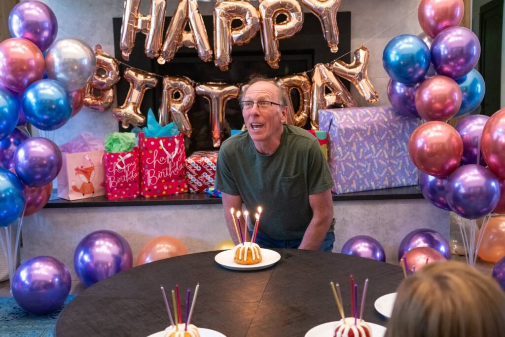 A joyful indoor birthday gathering features metallic balloons and a personalized Happy Birthday sign.