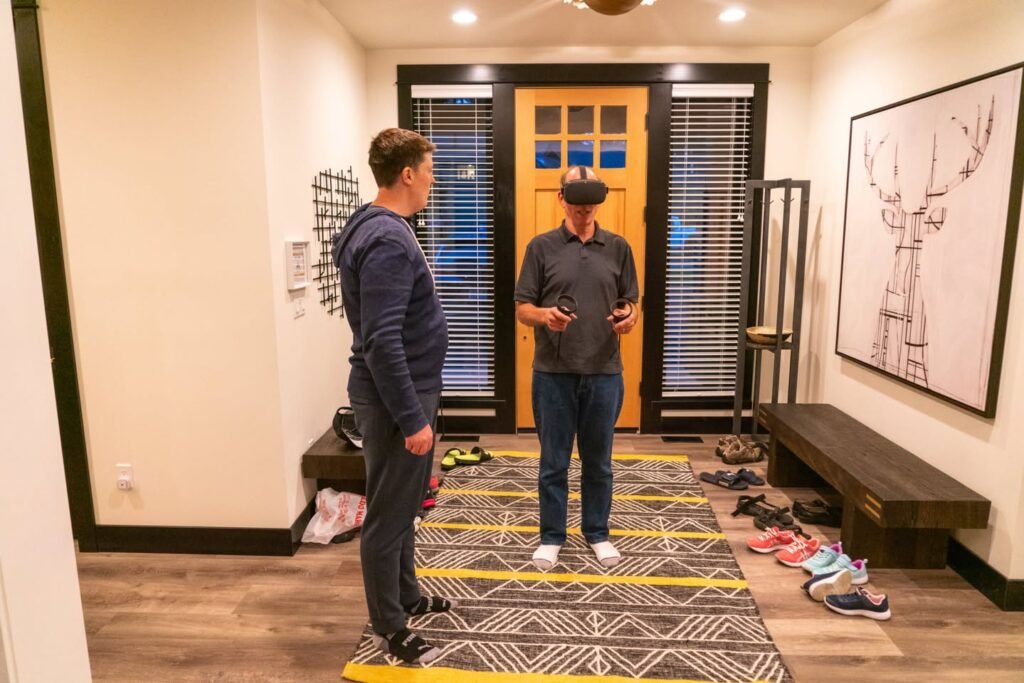 A person wearing a VR headset stands on a motion floor mat while another observes from the side.