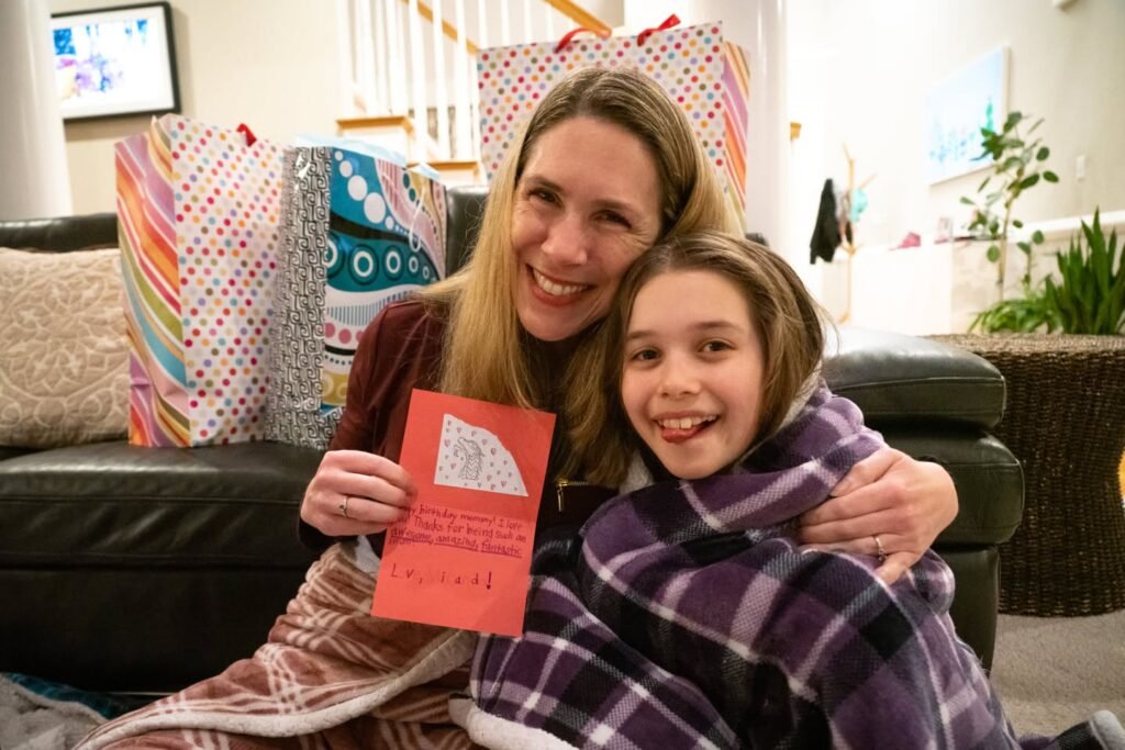 Two people sitting on a couch opening gifts surrounded by colorful wrapping paper and a greeting card.