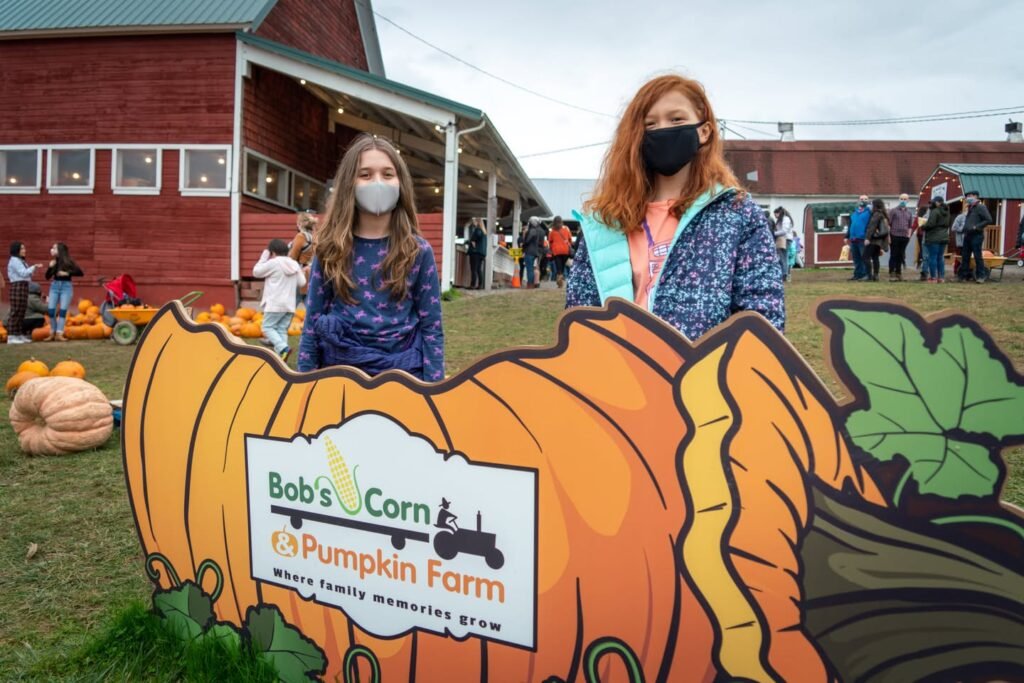 A wooden pumpkin sign at Bob’s Corn and Pumpkin Farm, with a red barn in the background.