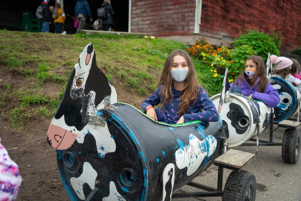 Children ride a whimsical painted boat designed to look like a Holstein cow during an outdoor event.
