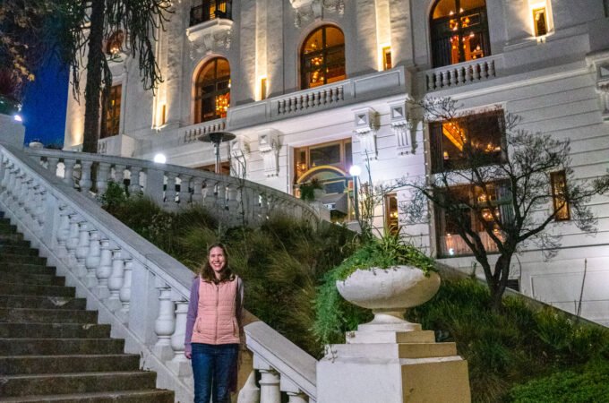 The Philippine General Hospital building is illuminated at dusk, with a person standing on the grand staircase.