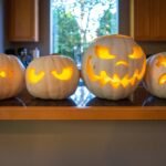 19th Anniversary A row of four carved pumpkins with glowing faces displayed on a wooden kitchen counter.
