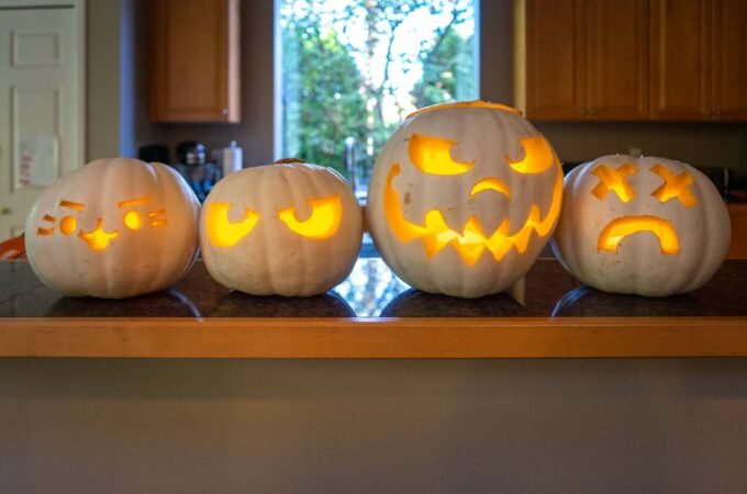 A row of four carved pumpkins with glowing faces displayed on a wooden kitchen counter.