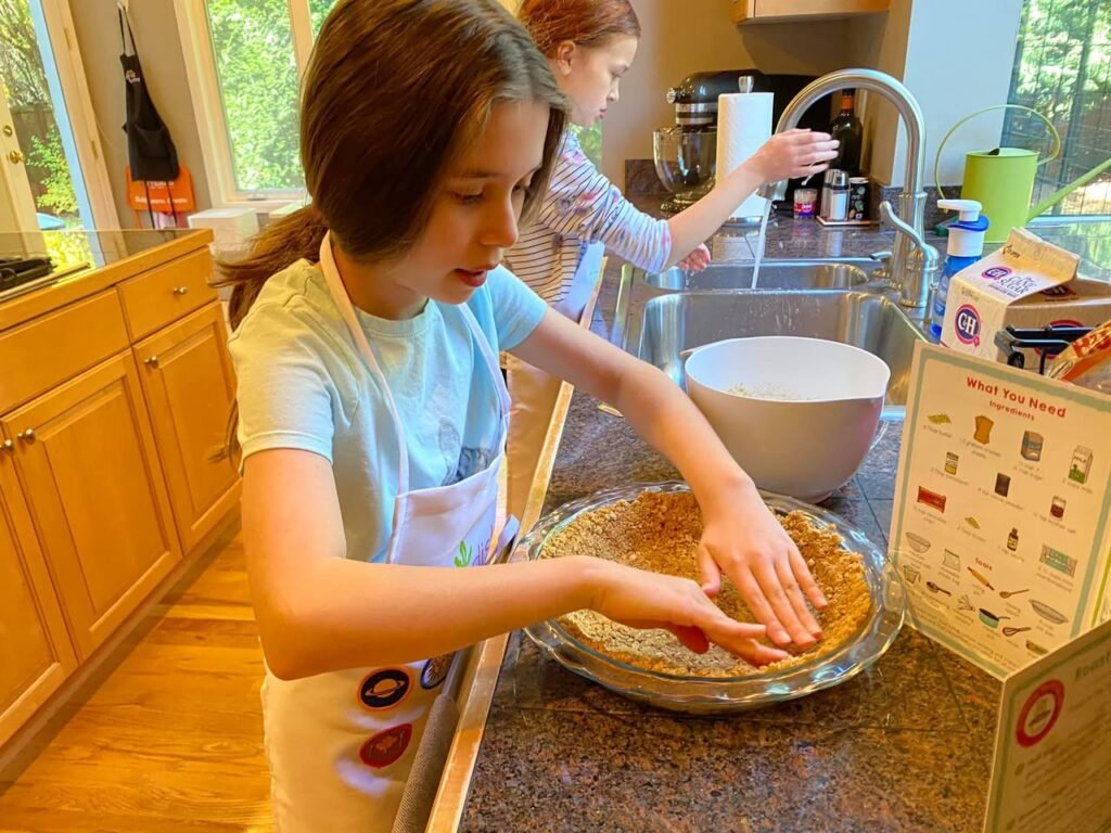 Children in an apron and shirt working on a pie crust in a PNY home kitchen.