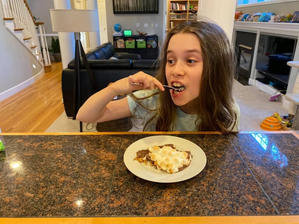 A person enjoys a plate of food with whipped toppings on a granite countertop in a cozy home setting.