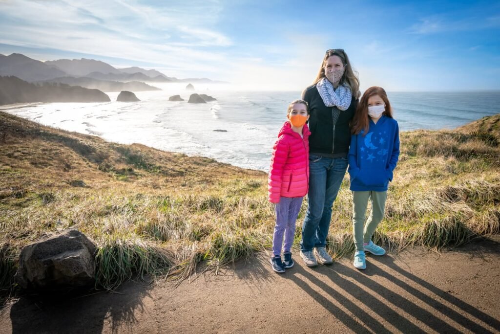 A family poses on a grassy cliff overlooking the Pacific Ocean. The distant rocky outcrops are partially shrouded in morning mist.