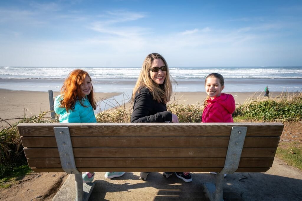 A family enjoying the Pacific Northwest coast, seated on a bench with a beach backdrop.