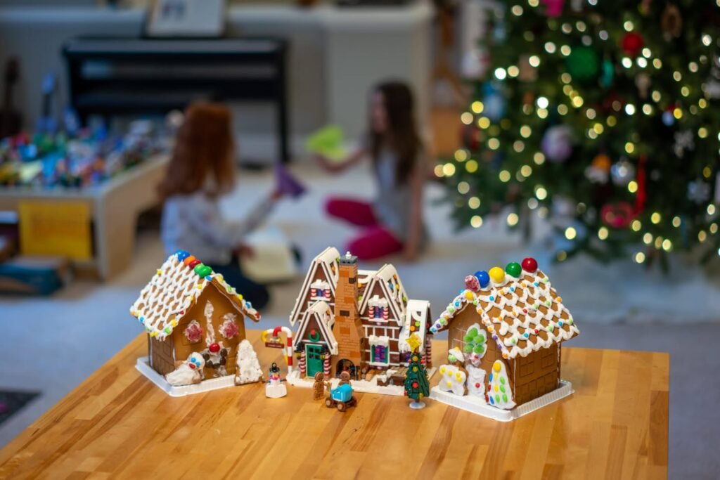 Delicate gingerbread houses adorn a wooden table with a festive Christmas tree and indoor scene in the background.