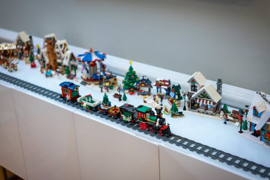 A detailed model train travels through a snowy winter village scene with structures and trees.