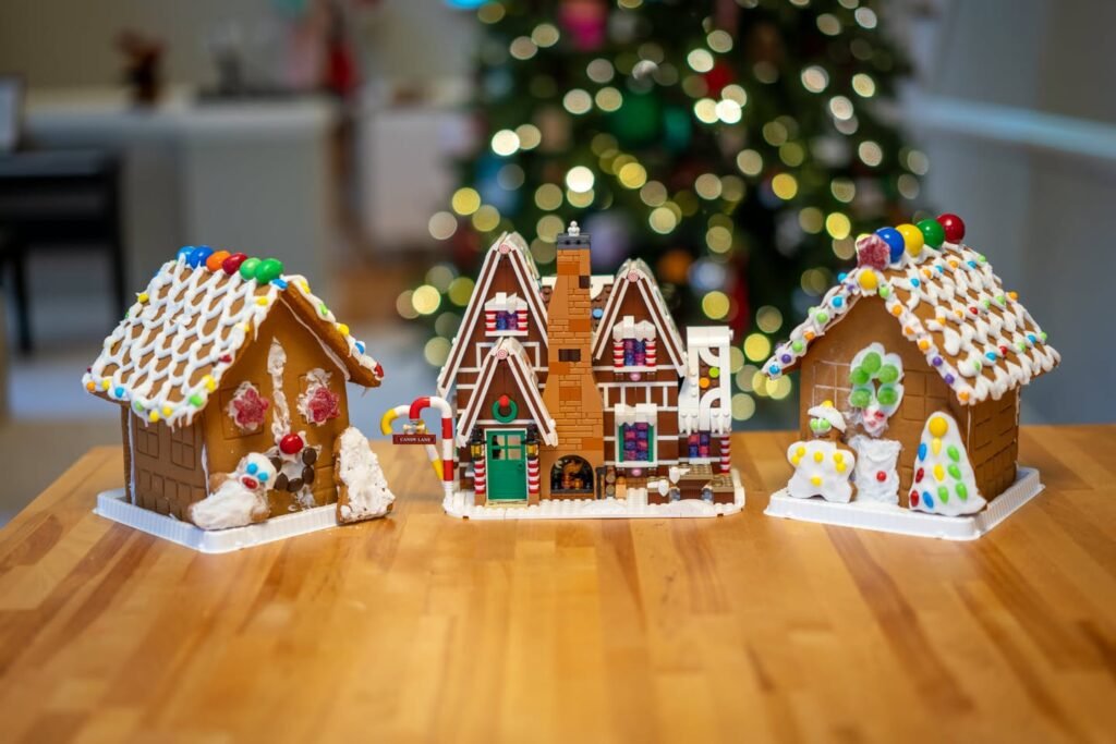 Three elaborately decorated gingerbread houses on a wooden surface with a Christmas tree in the background.