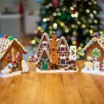Suncadia Winter Getaway Three elaborately decorated gingerbread houses on a wooden surface with a Christmas tree in the background.