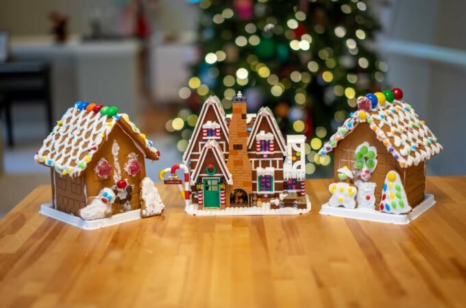 Three elaborately decorated gingerbread houses on a wooden surface with a Christmas tree in the background.