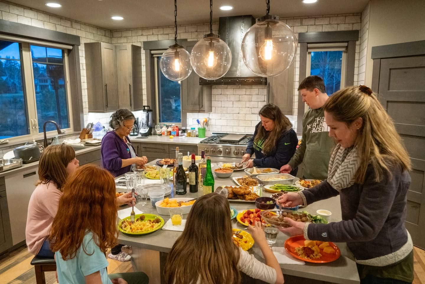 Suncadia Winter Getaway A group of people gathered around a large kitchen island enjoying a meal together in a modern kitchen.