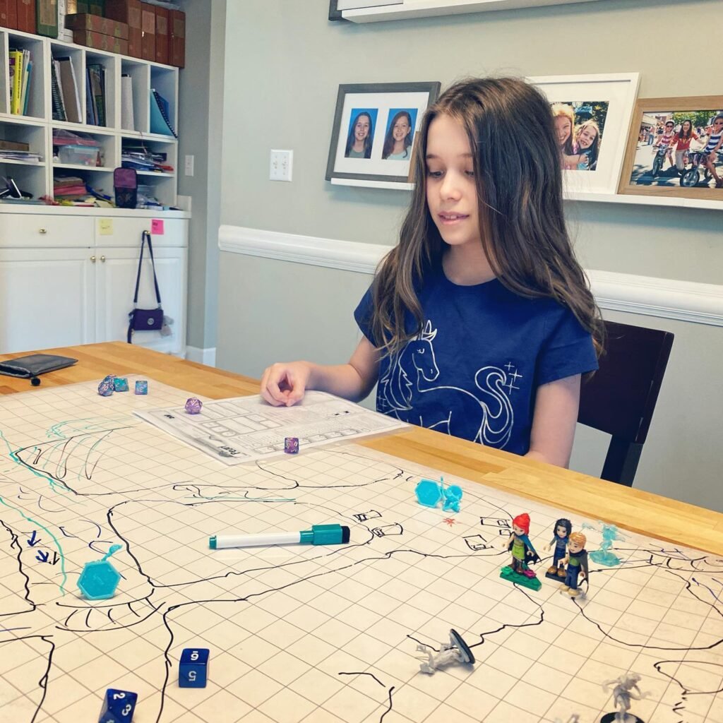 A person in a blue shirt plays a map-based board game at the kitchen table.
