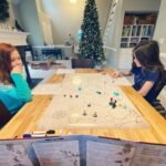 Suncadia Winter Getaway Children playing a board game at a table with a decorated Christmas tree in the background. A cozy holiday scene in a modern home.