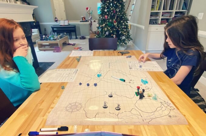 Children playing a board game at a table with a decorated Christmas tree in the background. A cozy holiday scene in a modern home.