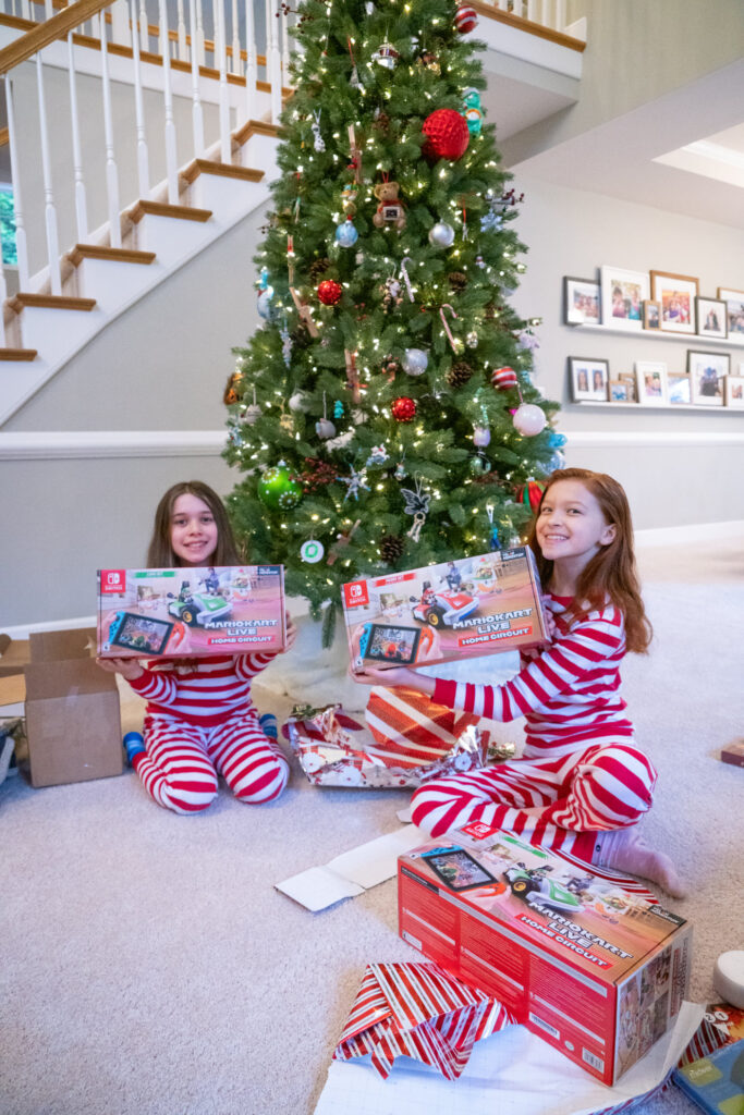 Two people in matching striped pajamas holding gifts in front of a Christmas tree.