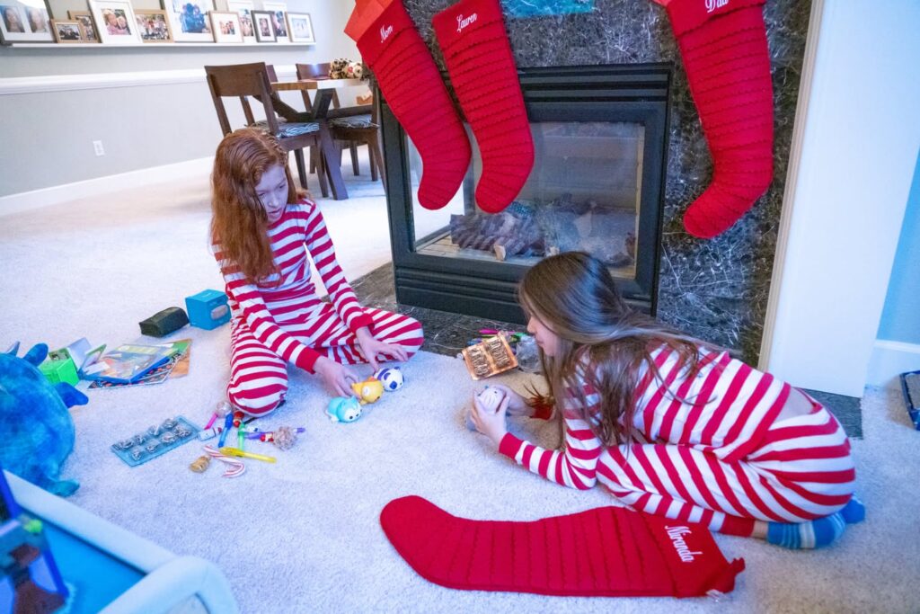 Two children in red and white striped pajamas playing on the floor. A red Christmas stocking hangs from the fireplace nearby.