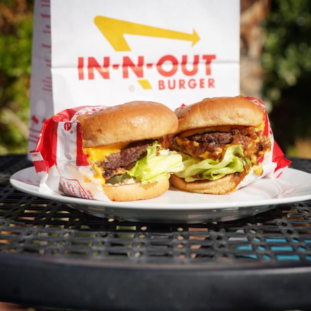 A close-up of an In-N-Out double cheeseburger on a plate with the-brand's menu in the background.