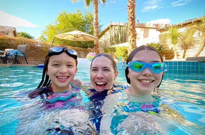 People wearing goggles in a clear blue pool with palm trees and desert landscaping in the background.