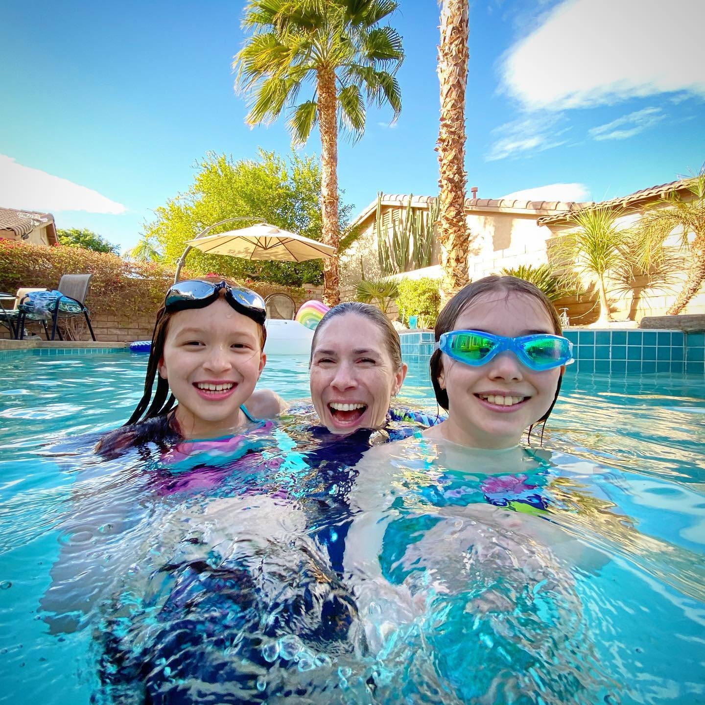 SoCal New Year People wearing goggles in a clear blue pool with palm trees and desert landscaping in the background.