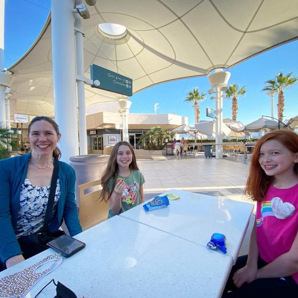 People enjoying a sunny day at an outdoor plaza with palm trees and modern architecture.