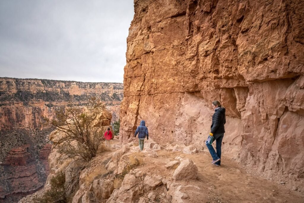 People hiking along a rocky trail next to a tall canyon wall.