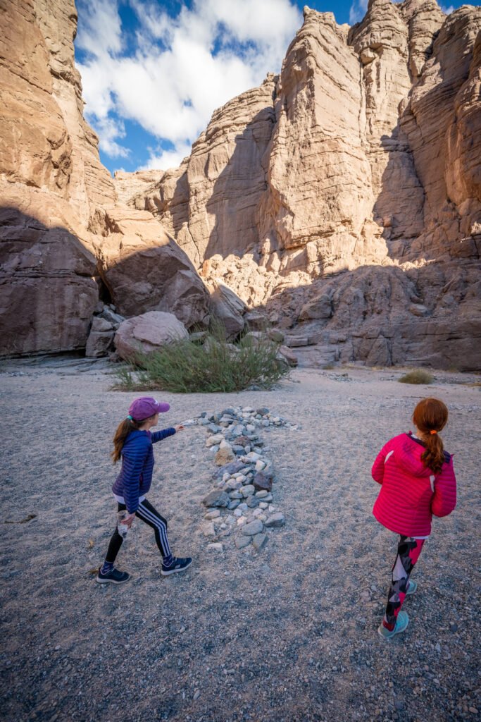 Two children exploring a rugged landscape with towering rock formations under a bright blue sky.