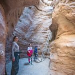 Anza-Borrego Sculptures Four hikers explore a narrow slot canyon with towering sandstone walls.