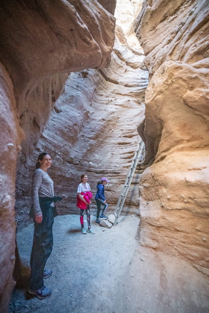 Four hikers explore a narrow slot canyon with towering sandstone walls.