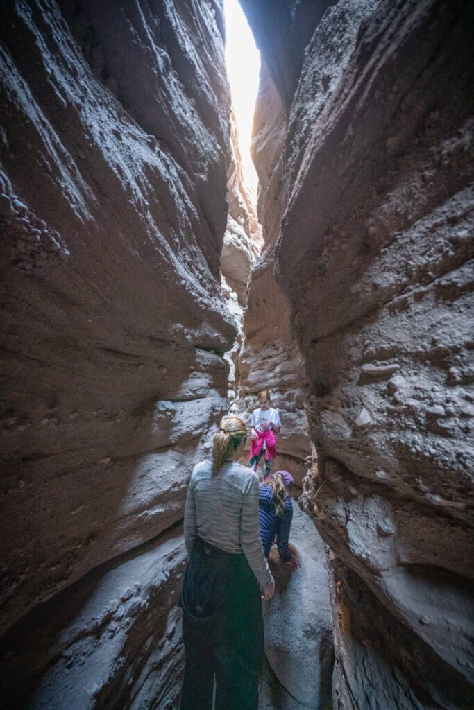 Hikers navigating a narrow slot canyon with snow-dusted rock walls. Looking down from the canyon rim at a scenic trail.