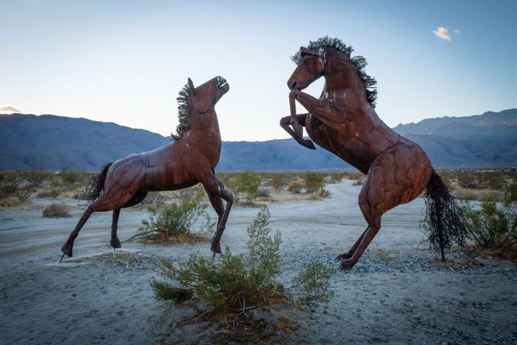 Two reering mustangs in a desert landscape with distant mountains under a clear sky.