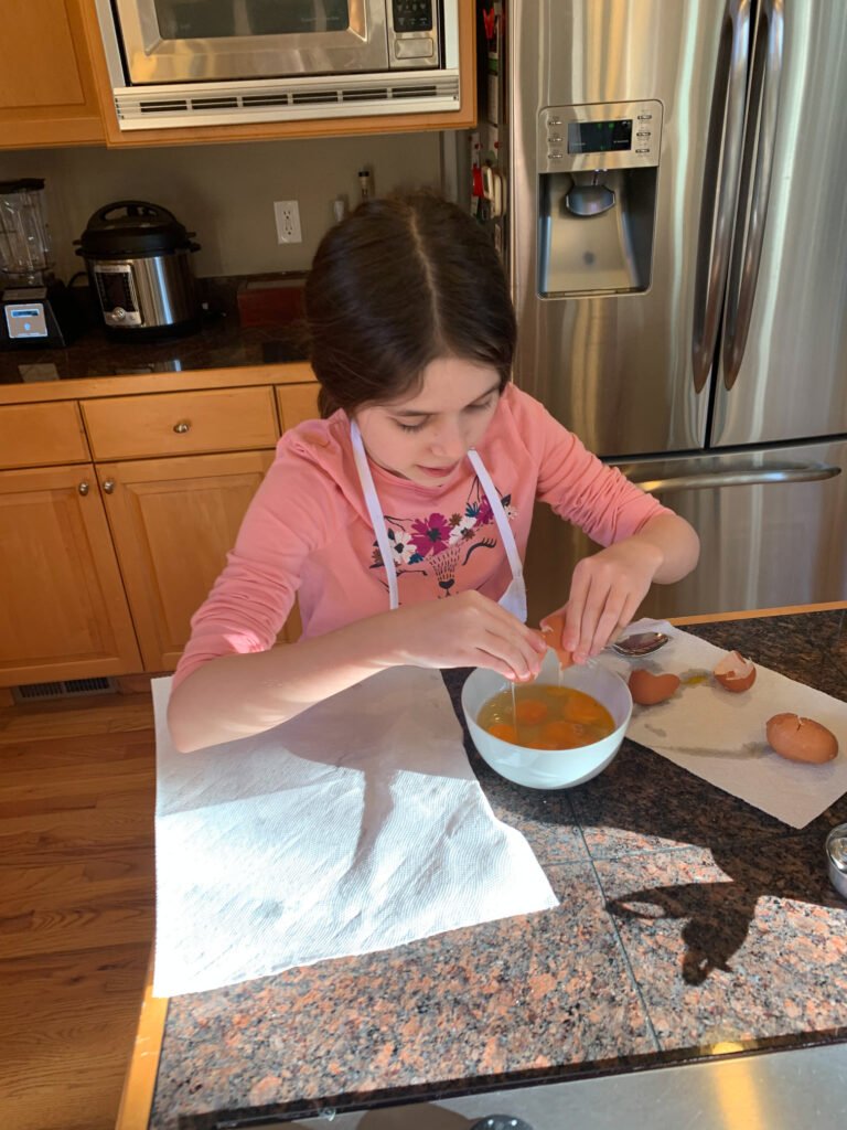 A child wearing an apron dyes Easter eggs at a kitchen counter.