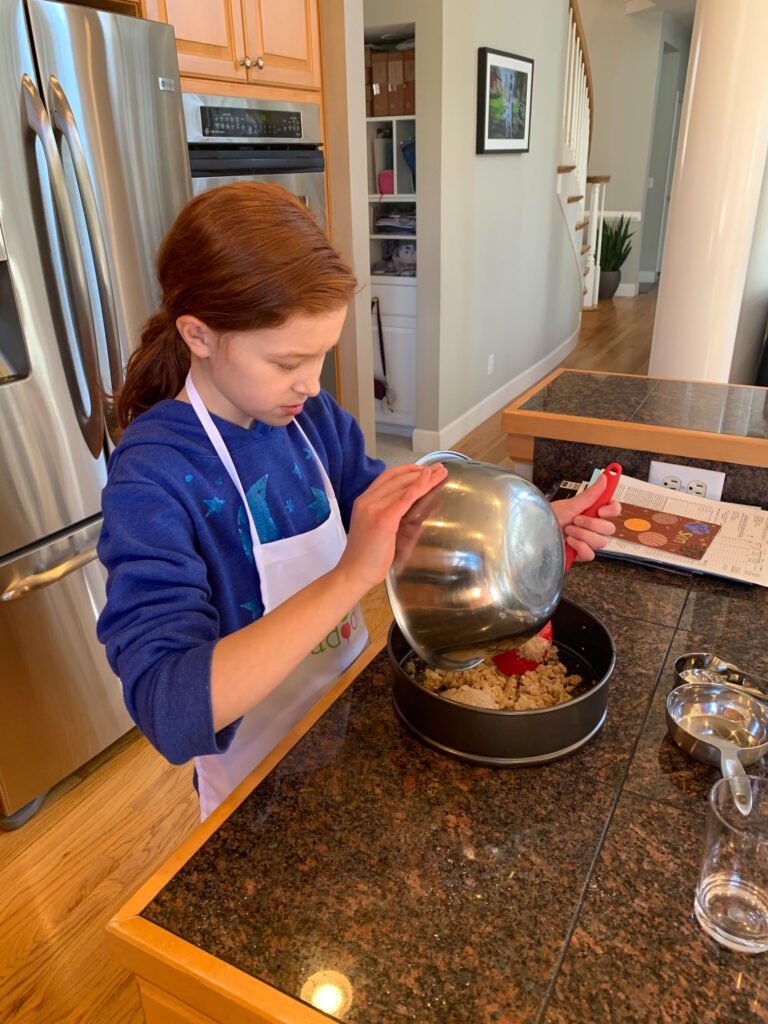 A person pours ingredients into a mixing bowl from a metal pot in a modern kitchen.