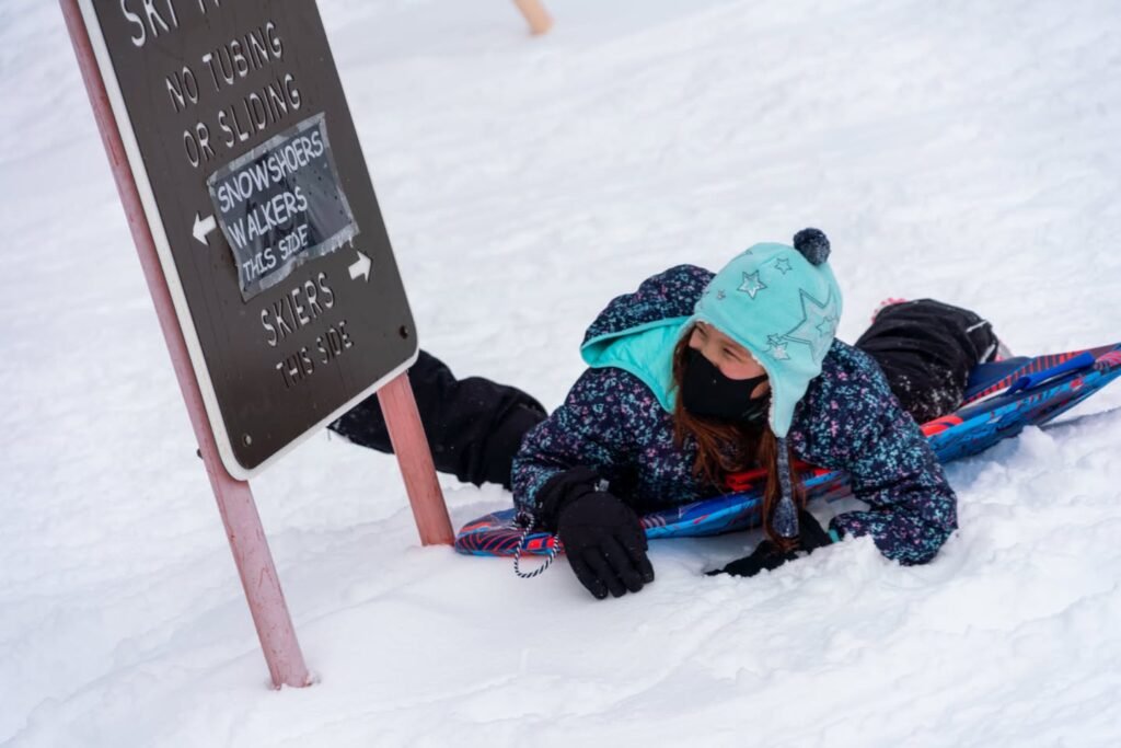 A close-up of a sign and a person lying on the snow next to a blue plastic tube.