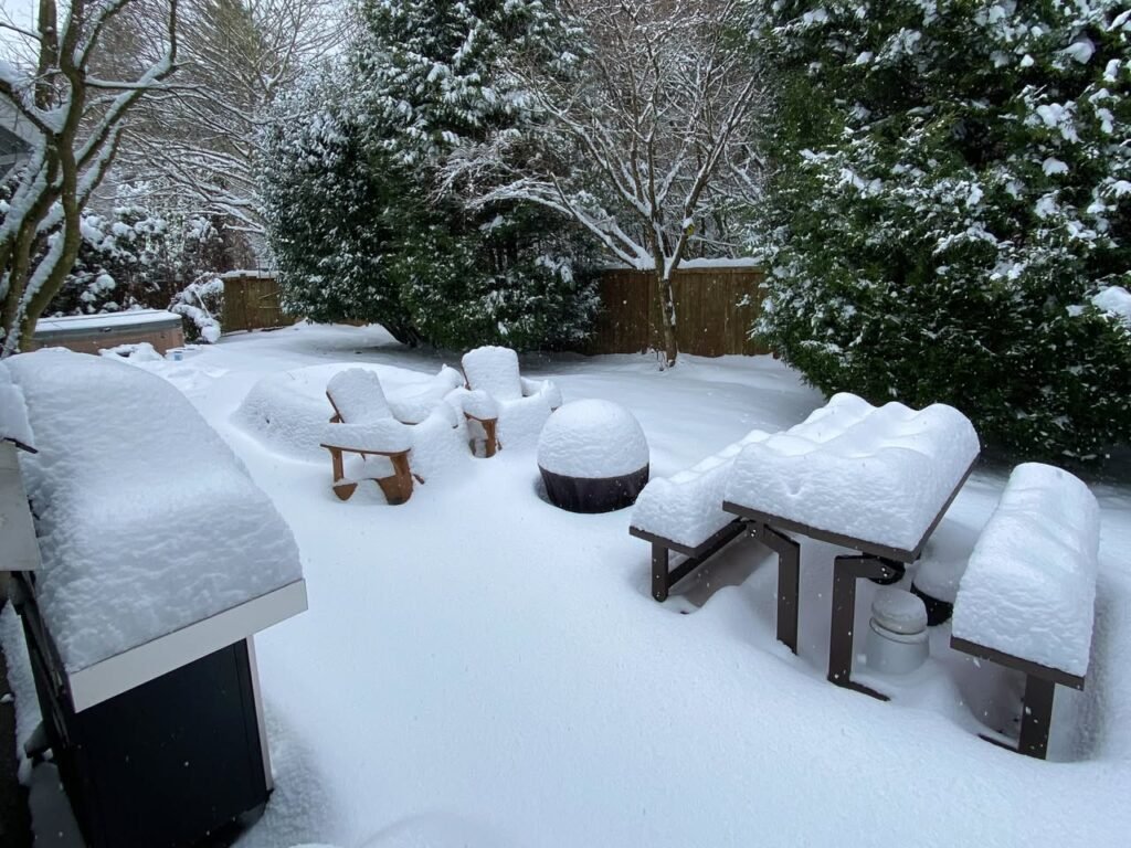 A serene winter scene featuring outdoor furniture and trees blanketed in fresh snow.