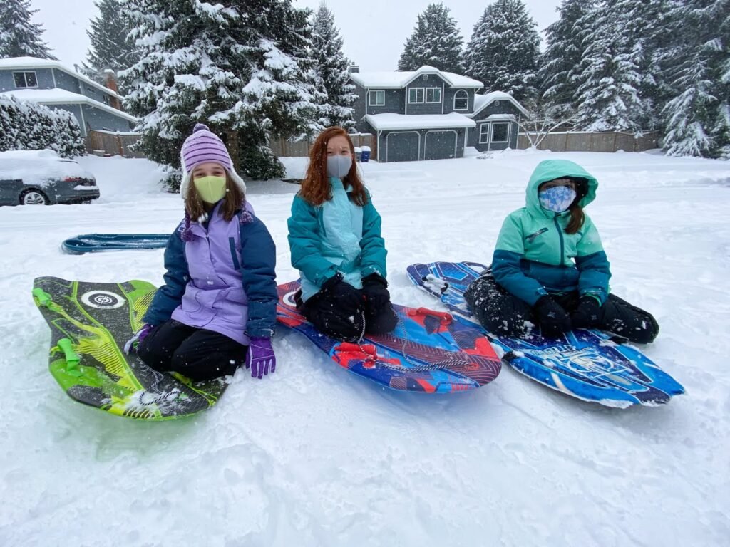 Three individuals enjoying snow tubing in a snowy backyard. Colorful tubes add vibrancy to the winter landscape.