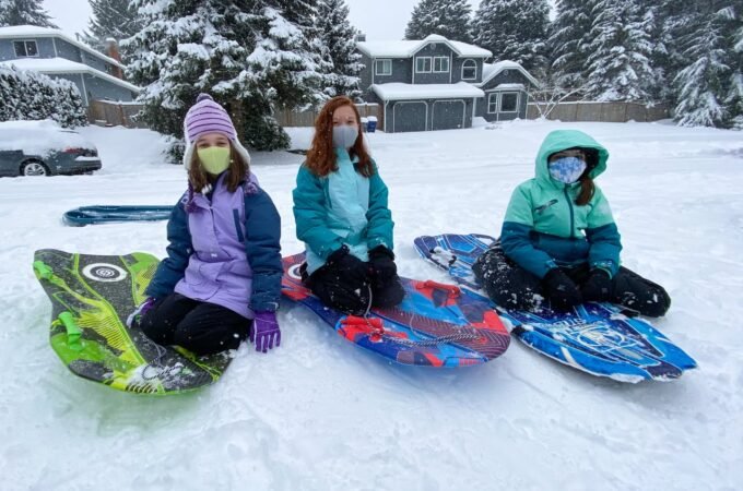 Three individuals enjoying snow tubing in a snowy backyard. Colorful tubes add vibrancy to the winter landscape.