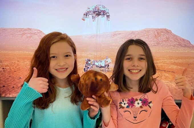 Two children giving a thumbs up while watching a science fiction movie with a desert planet.
