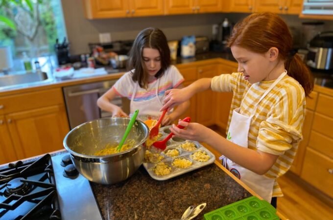 Two children bake cookies in a home kitchen with wooden cabin.