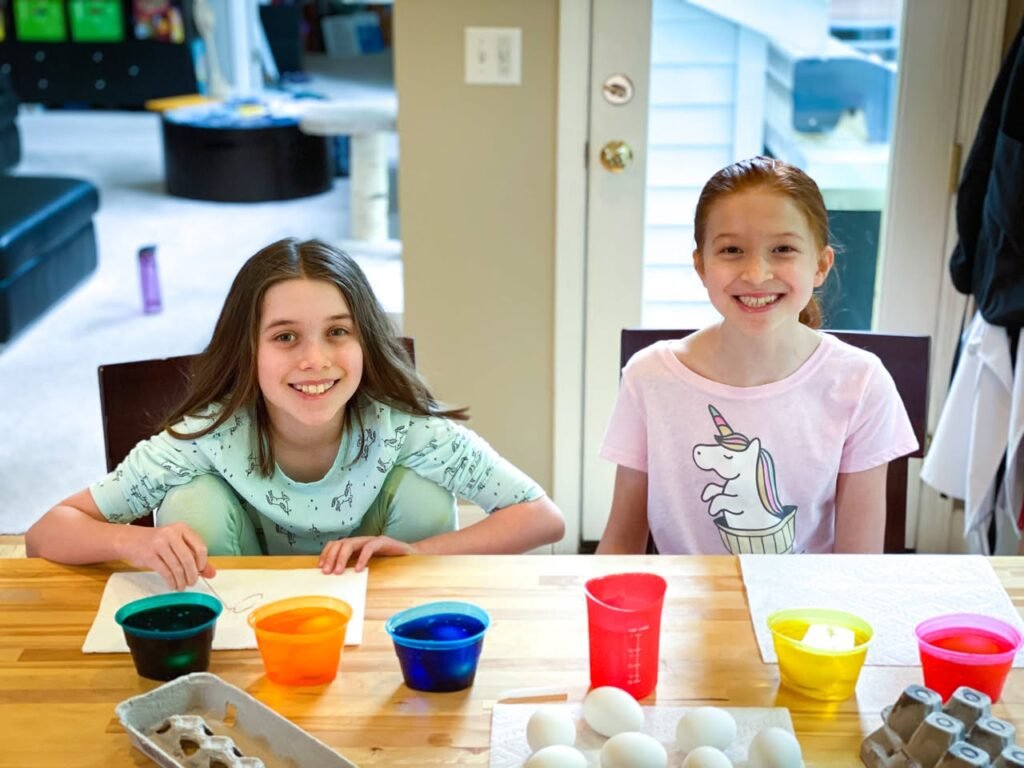 Two children sitting at a kitchen table with colored dyes and eggs.