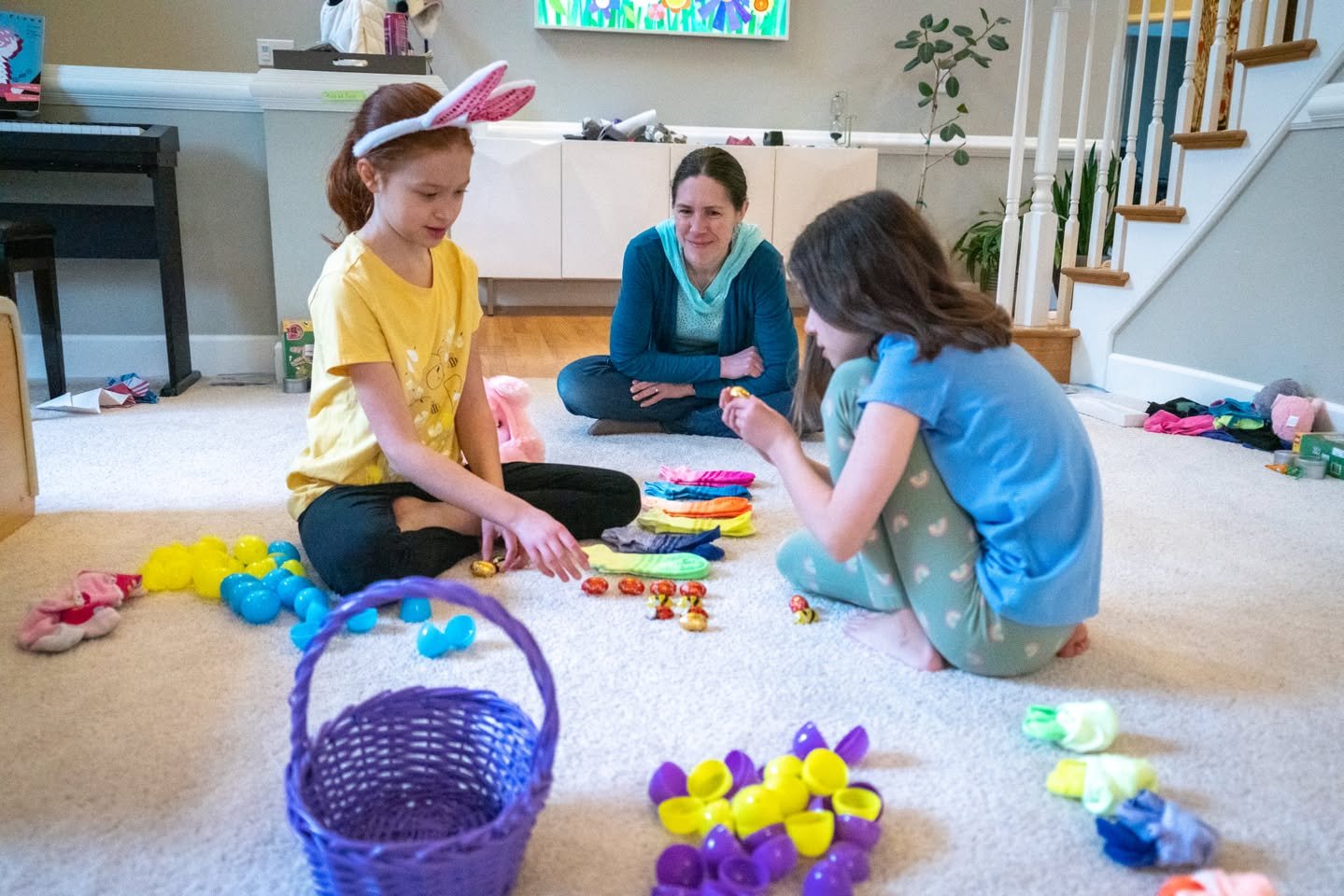 Happy Easter Children and an adult collecting dyed Easter eggs in a cozy living room with a purple basket and colorful eggs on the floor.