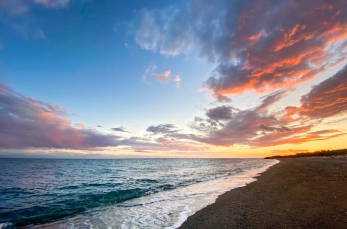 A serene beach scene in the Pacific Northwest at sunset, with waves rolling onto the shore. The sky is filled with pink and orange clouds.