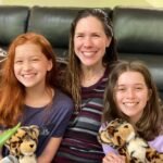 A family of three smiles on a black leather couch, each holding a stuffed tiger toy.